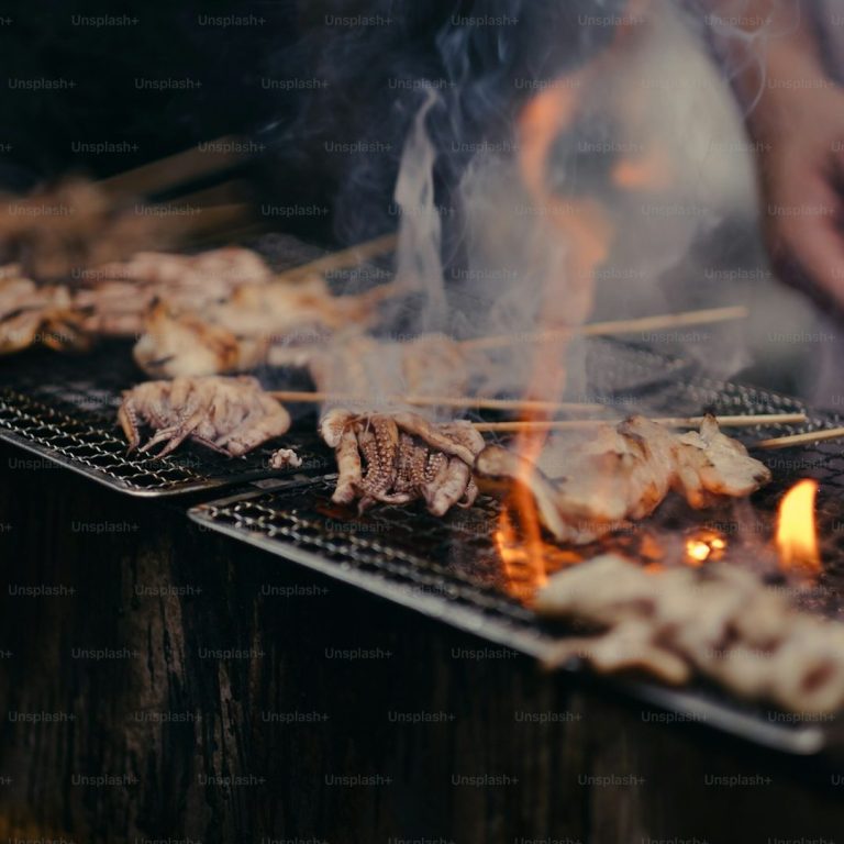 Gegrillte Spieße mit Rauch und Flammen, Hand greift nach einem Spieß.